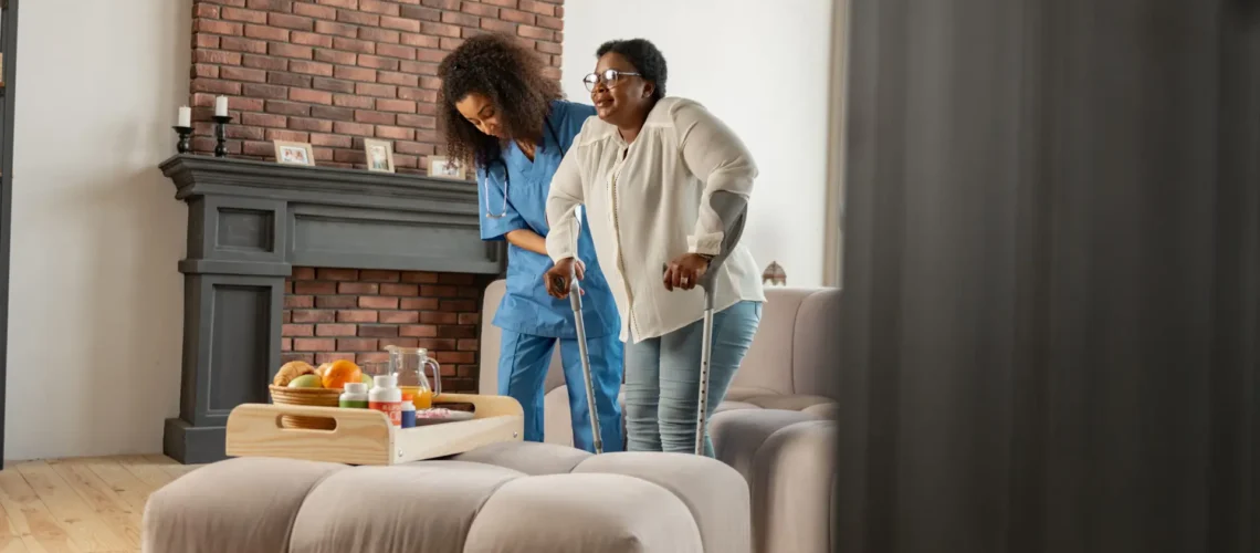 First steps. Aged woman wearing glasses feeling happy making first steps with crutches standing near nurse
