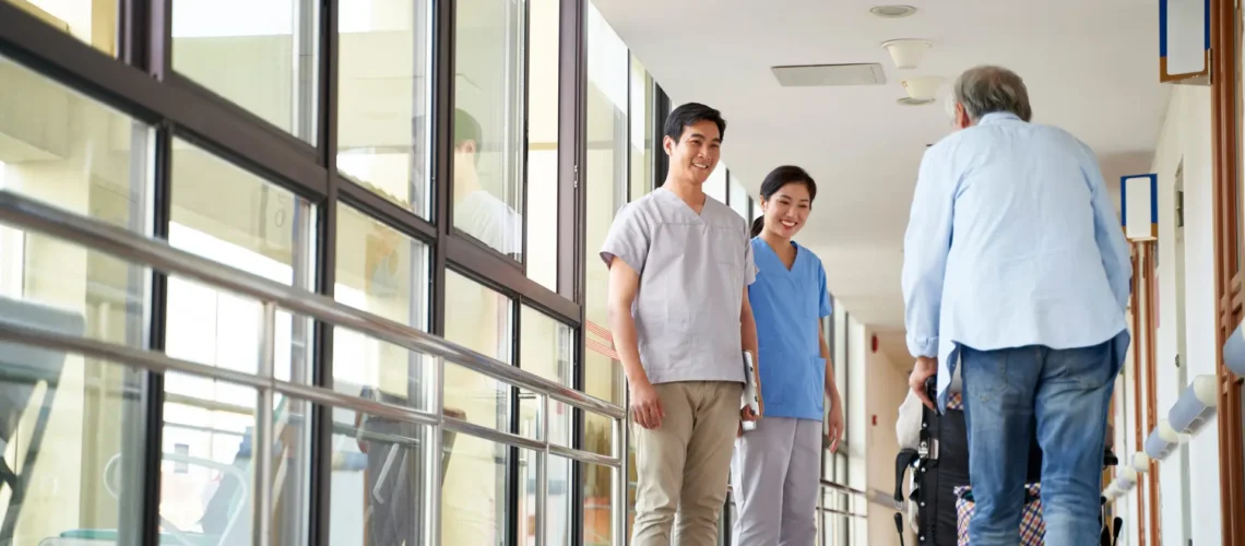happy young asian physical therapists greeting residents in hallway of nursing home